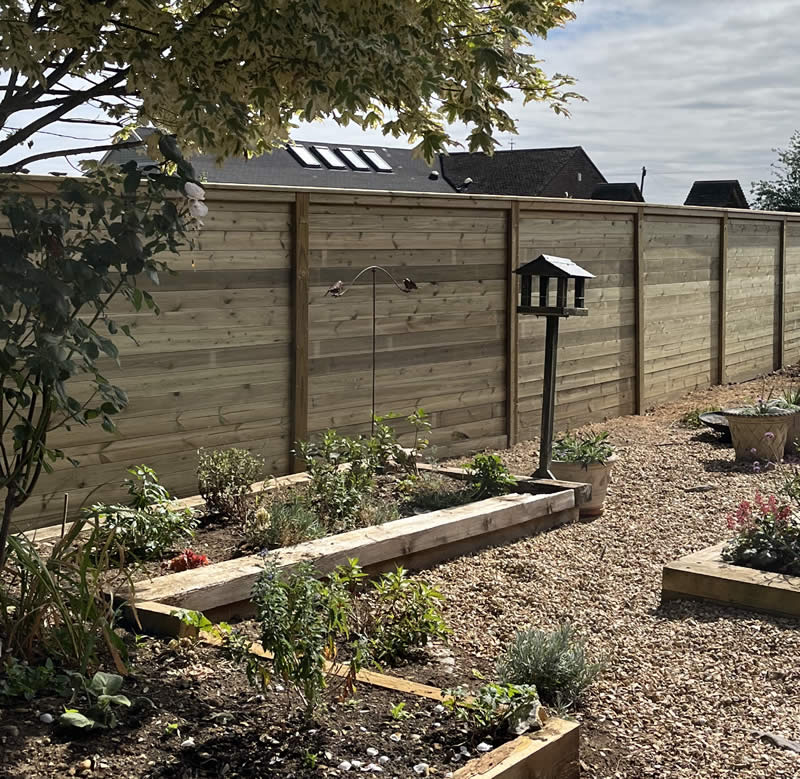 Slatted screen fencing in a garden setting, showcasing wooden panels, flower beds, and a bird feeder, illustrating decorative and functional uses for outdoor spaces.